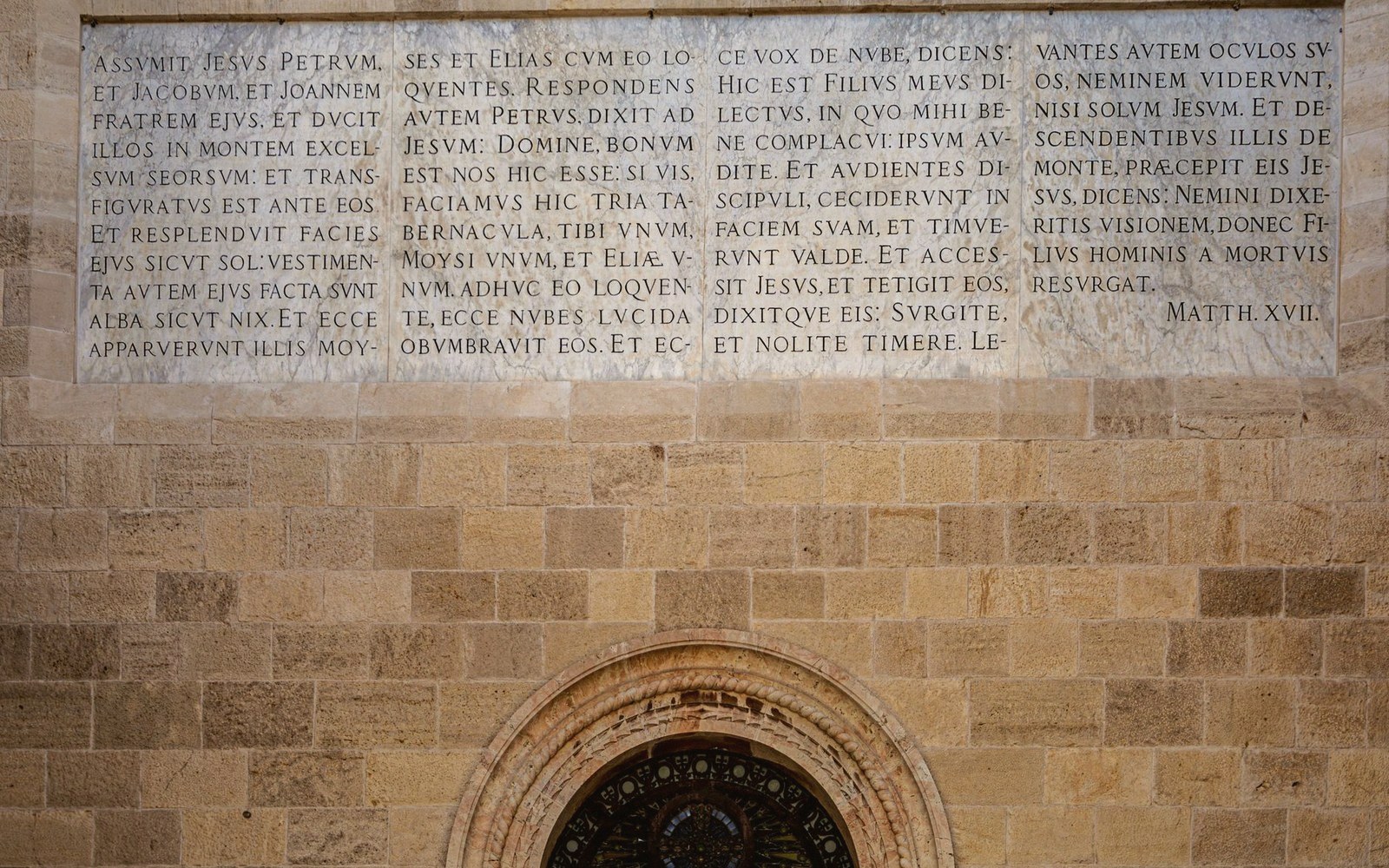 Latin inscription of Matthew 17 carved into a church's stone facade above an arched window